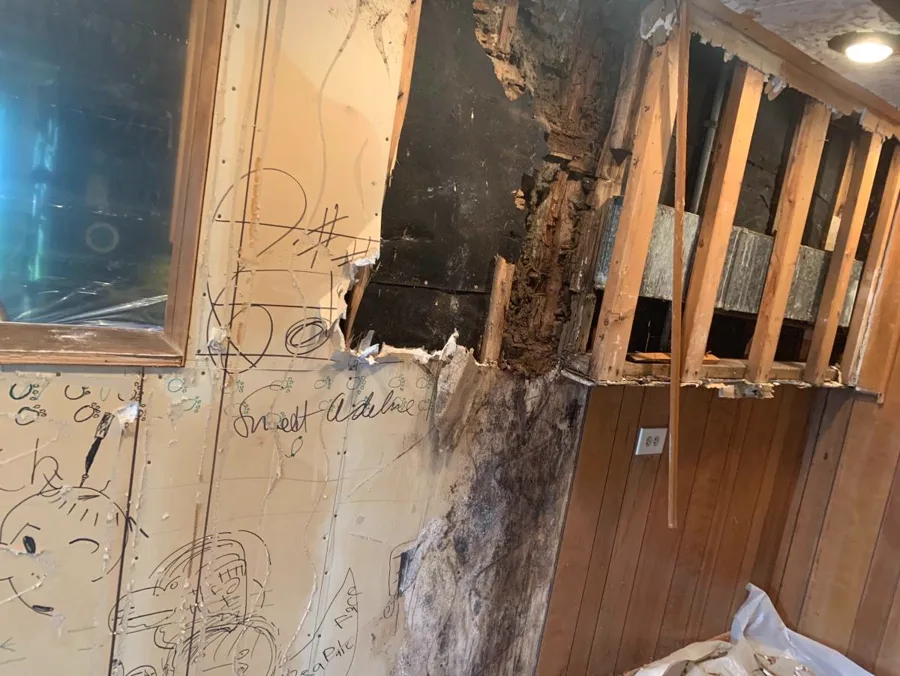 Water-soaked drywall cut away to expose wall studs before replacement
